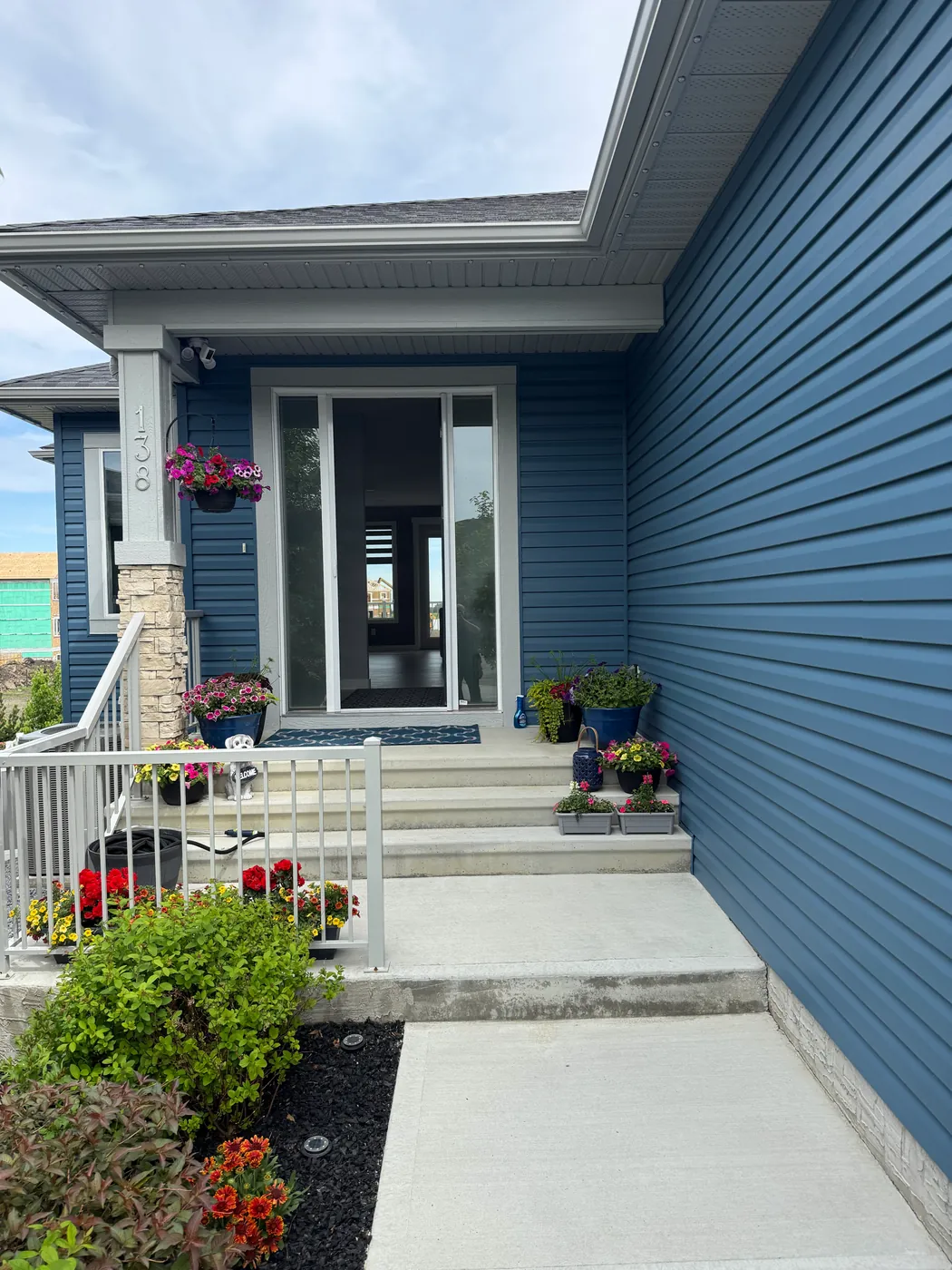 Blue-sided Edmonton home with a Mirage retractable screen on the glass front entry door and flower-lined steps
